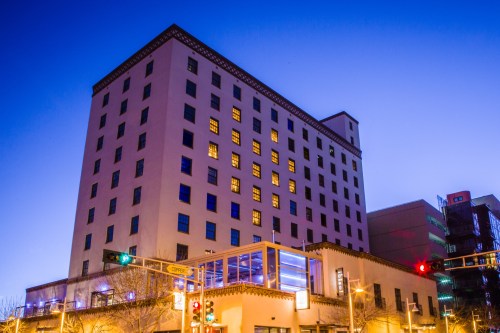 A tall building at dusk, with illuminated windows and a clear blue sky in the background.