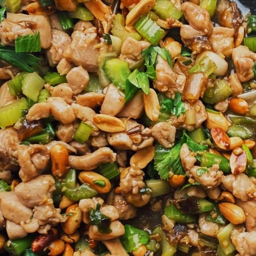 A close-up of a stir-fried dish featuring chicken, celery, and peanuts in a savory sauce.