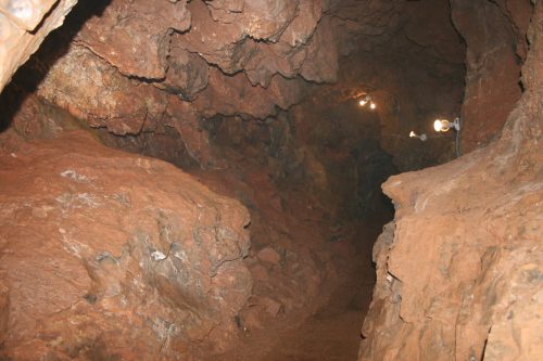 A dimly lit cave interior with rocky walls and a narrow path, illuminated by a few overhead lights.
