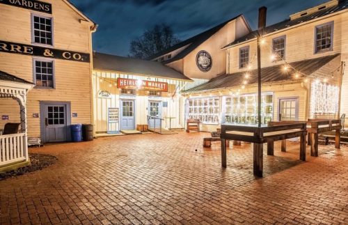 A charming market entrance with string lights, brick pavement, and historic buildings under a twilight sky.