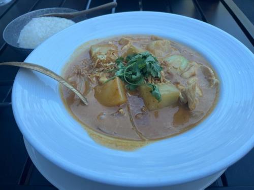 A bowl of curry with chicken and potatoes, garnished with cilantro, served with a side of rice.