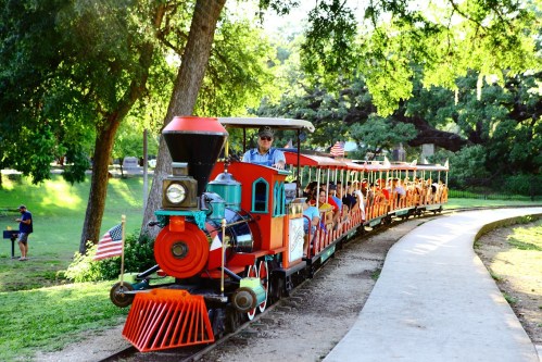 A colorful miniature train with passengers rides along a path in a lush green park.
