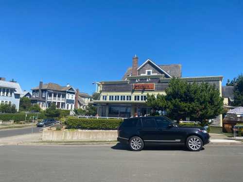 A black SUV parked in front of a charming restaurant with a green lawn and historic buildings under a clear blue sky.