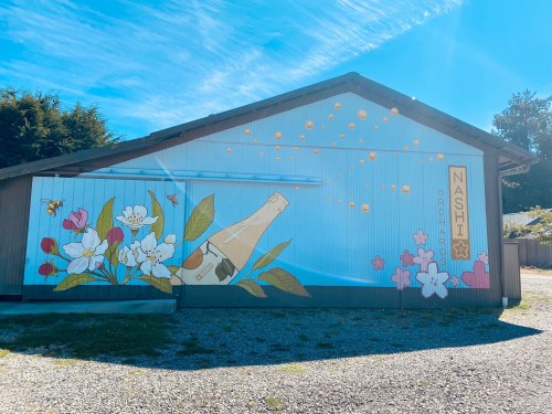 A mural on a building featuring a bottle, flowers, and bubbles against a blue sky.