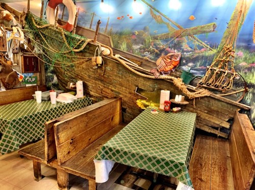 Interior of a themed restaurant featuring wooden tables and a boat replica against a colorful underwater mural.