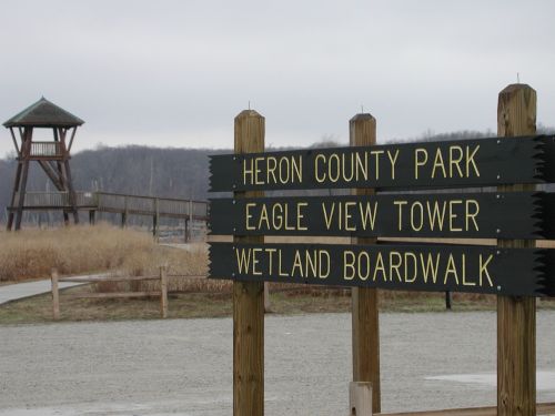 Signpost for Heron County Park, featuring Eagle View Tower and Wetland Boardwalk, with a lookout tower in the background.