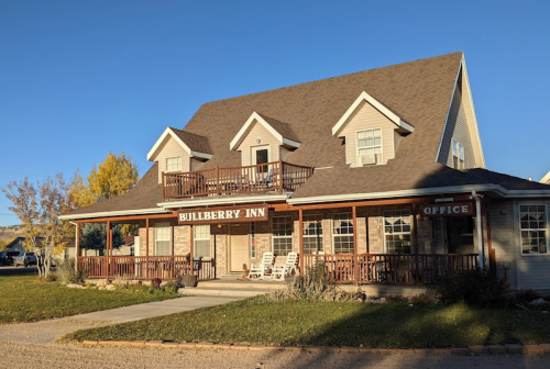 A charming two-story inn with a porch, sign reading "Bullberry Inn," surrounded by greenery and clear blue skies.