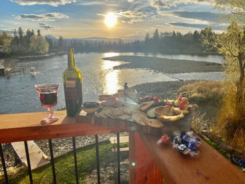 A scenic sunset over a lake, featuring a wine bottle, glass, and a platter of snacks on a wooden table.