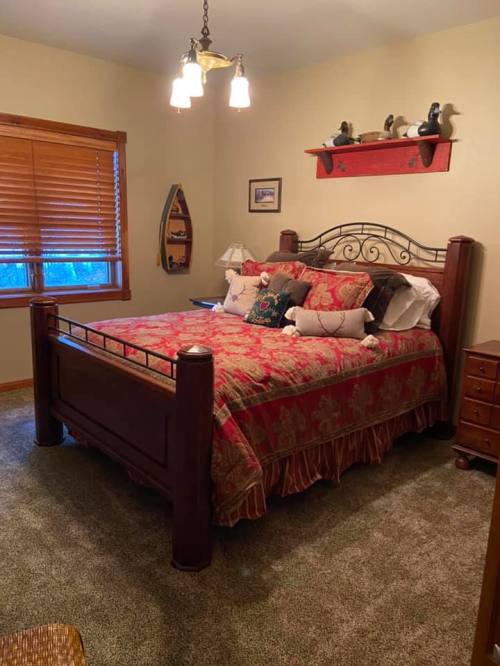 Cozy bedroom with a wooden bed, colorful bedding, and decorative pillows, featuring a window and warm lighting.