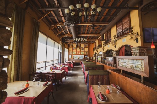 Interior of a cozy restaurant with wooden beams, colorful artwork, and tables set with red tablecloths.