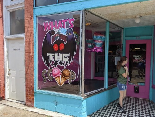 A colorful ice cream shop window with a large sign reading "What's the Scoop" and a girl standing outside.
