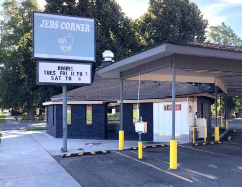 A small building with a sign reading "Jeb's Corner," featuring business hours and a drive-thru area.