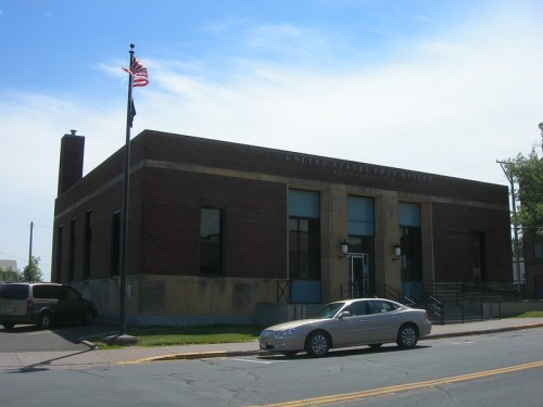A brick building with a flat roof, featuring a U.S. flag, labeled as the United States Post Office.