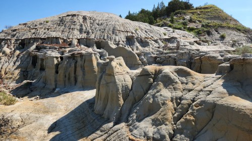 A rugged landscape of eroded rock formations and hills under a clear blue sky.