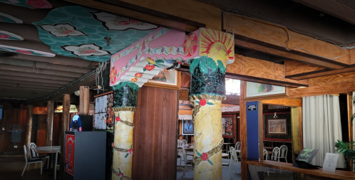 Colorful, artistic columns and a vibrant ceiling in a rustic restaurant interior with wooden beams and decor.