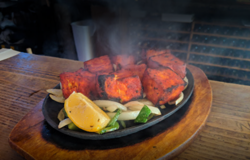 Sizzling platter of grilled marinated chicken, onions, and lemon, with steam rising from the hot surface.
