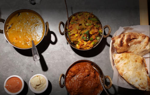 A table with three bowls of curry, naan bread, and two small bowls of sauces.