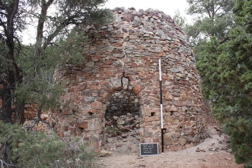 Stone structure surrounded by trees, featuring an arched entrance and a sign nearby.