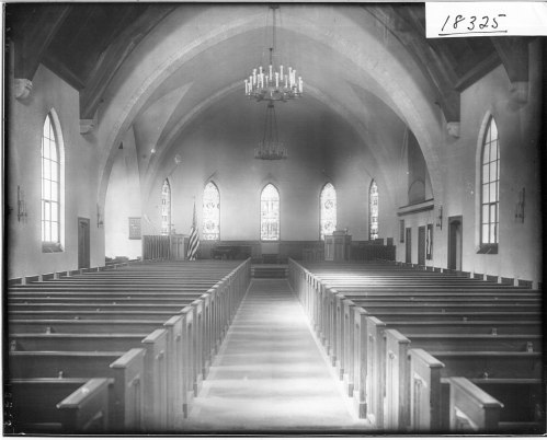 Interior of a church featuring wooden pews, arched ceilings, and stained glass windows.
