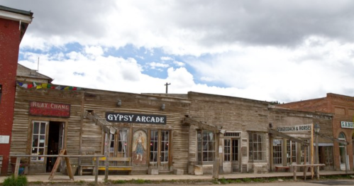 Historic wooden storefronts with signs for "Gypsy Arcade" and "Stables & Horses" under a cloudy sky.