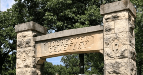 Stone archway with the words "Rochester Cemetery" engraved, surrounded by trees and greenery.