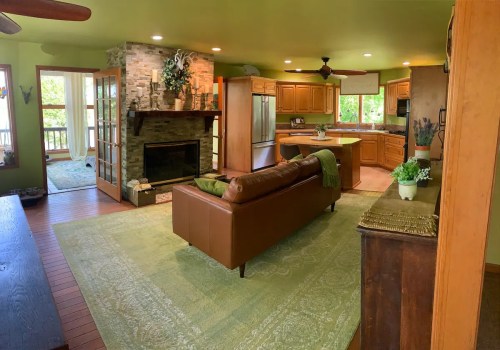 Cozy living room with green walls, a stone fireplace, and a brown leather sofa, featuring a view of the outdoors.