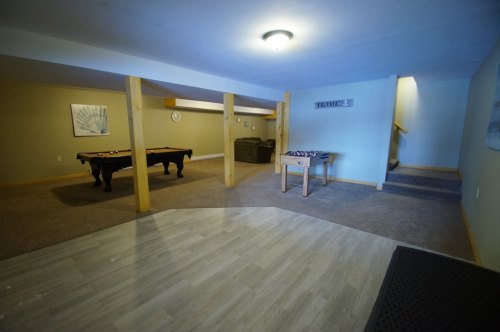 A spacious basement with a pool table, seating area, and stairs leading to an upper level.