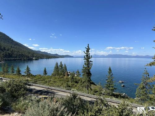 Scenic view of a calm lake surrounded by mountains and trees under a clear blue sky.