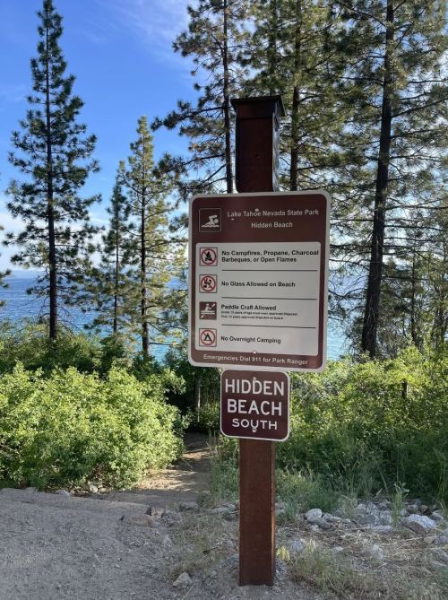 Sign at Hidden Beach, Lake Tahoe Nevada State Park, with rules and regulations for visitors, surrounded by trees.
