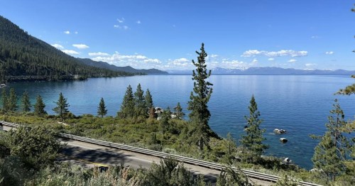 A serene view of a lake surrounded by trees and mountains under a clear blue sky.