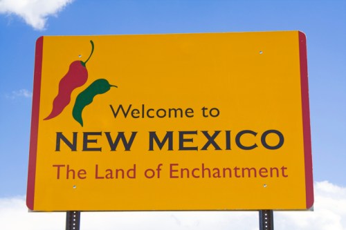 Welcome sign for New Mexico, featuring the text "The Land of Enchantment" and colorful chili pepper graphics.