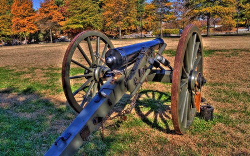 A historic cannon on wheels, set on a grassy field with colorful autumn trees in the background.