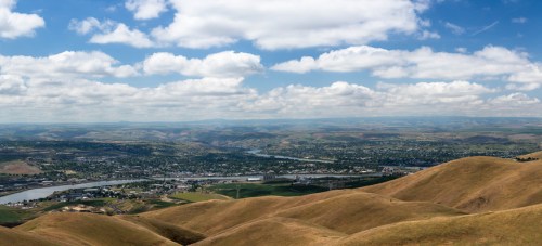 A panoramic view of rolling hills and a river valley under a partly cloudy sky.