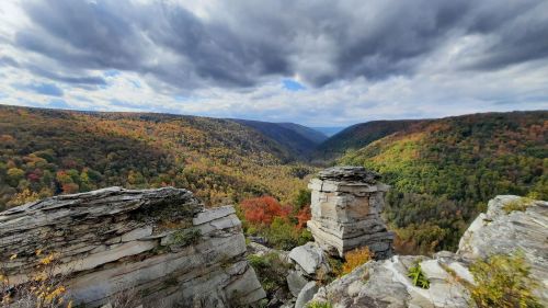 A scenic view of a valley surrounded by autumn foliage and rocky outcrops under a cloudy sky.