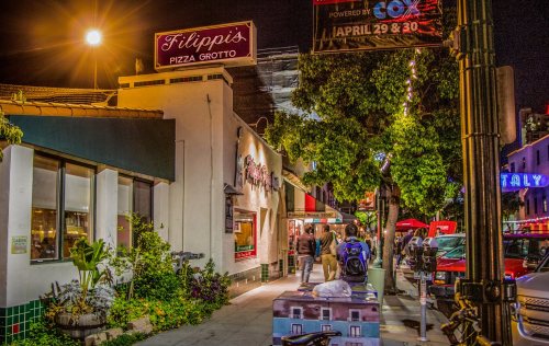 A lively street scene at night featuring Filippi's Pizza Grotto, with people walking and colorful lights illuminating the area.