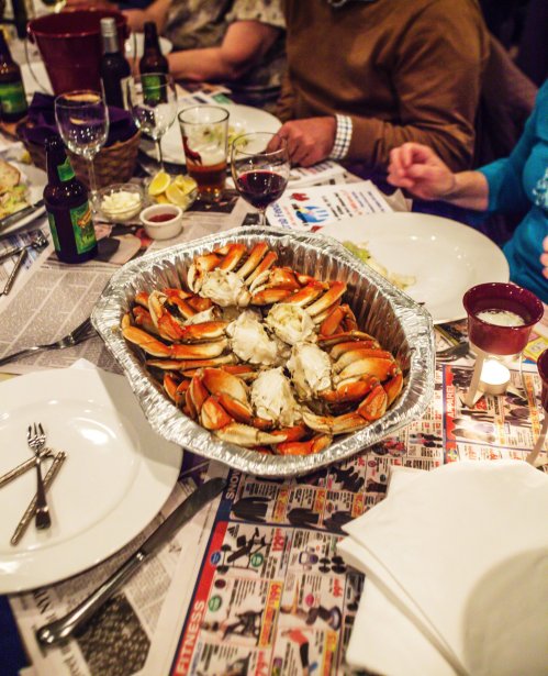 A large platter of crabs sits on a table covered with newspapers, surrounded by drinks and plates.