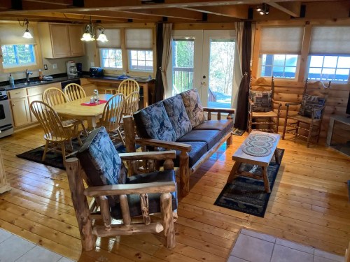 Cozy cabin interior with wooden furniture, a dining table, and large windows letting in natural light.