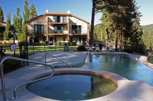 A serene outdoor pool area with a hot tub, surrounded by trees and a modern building in the background.