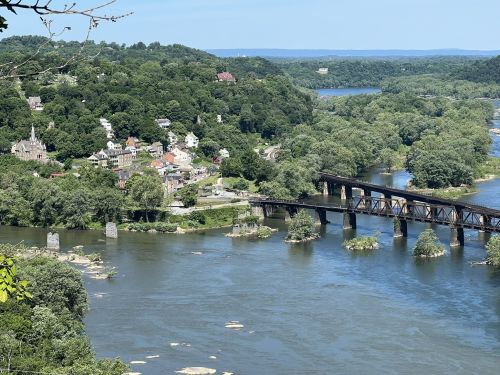 A scenic view of a river winding through lush greenery, with a small town and a railway bridge in the foreground.