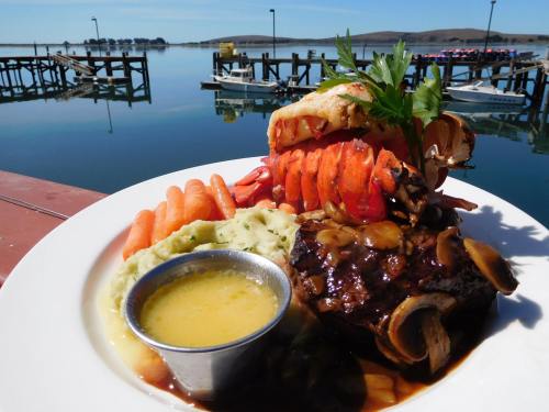 A plate of surf and turf featuring lobster, steak, mashed potatoes, and carrots, with a scenic waterfront view.