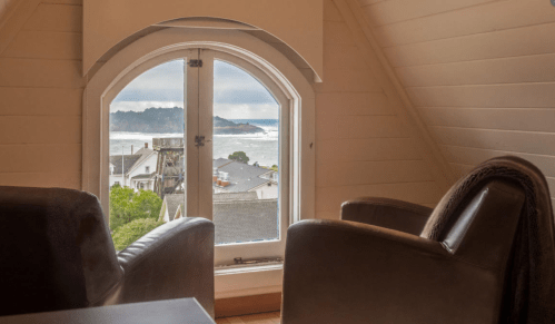 Cozy interior with two chairs, featuring a large arched window overlooking a coastal view and distant waves.