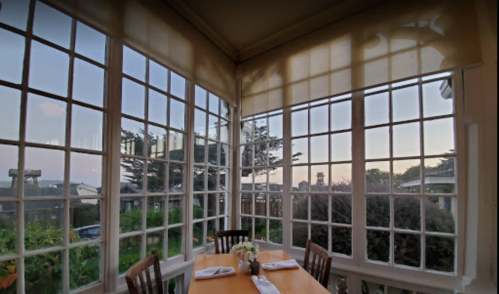 A cozy dining area with large windows, offering a view of the outdoors and a table set for two.
