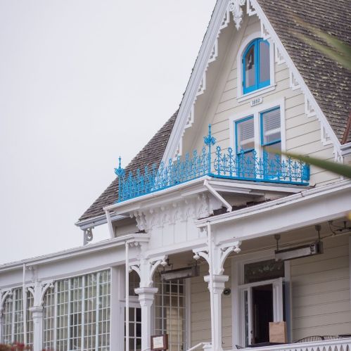 A charming Victorian-style house with a blue balcony and intricate white trim under a cloudy sky.