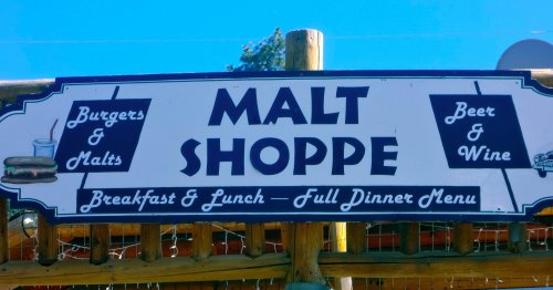 Sign for "Malt Shoppe" featuring burgers, malts, beer, and wine, with breakfast, lunch, and dinner options.