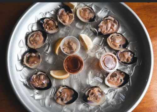 A platter of fresh oysters on ice, garnished with lemon wedges and dipping sauces in small cups.