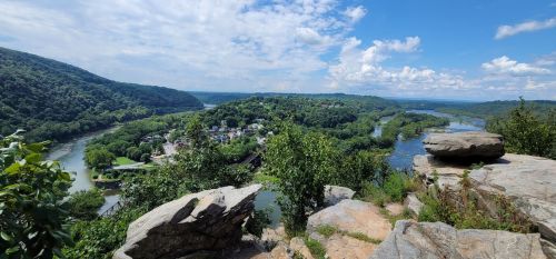 A scenic view of a river winding through lush green hills under a blue sky with scattered clouds.