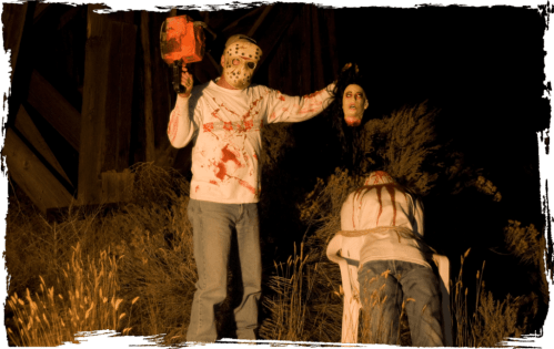 A masked figure holds a chainsaw and a severed head, with a bound person sitting in a chair in a dark, eerie setting.