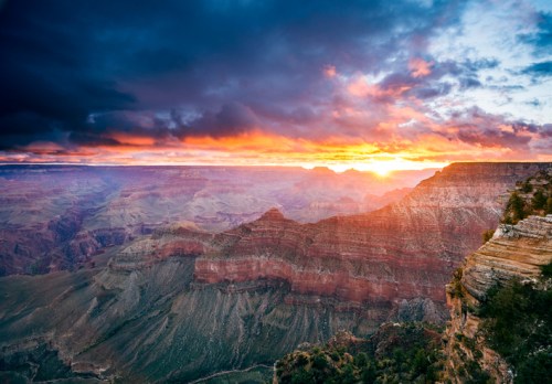 A stunning sunset over the Grand Canyon, with vibrant colors illuminating the rocky landscape and dramatic clouds.