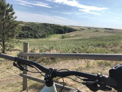 A bike handlebar in the foreground with a scenic view of green hills and a blue sky in the background.