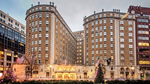 Historic hotel building with two curved towers, adorned with flags and festive decorations, set in an urban environment.